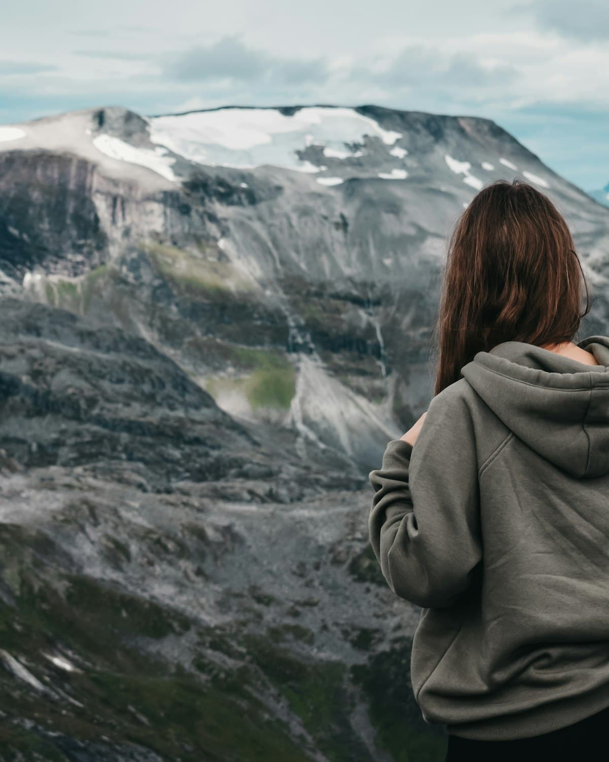 Person in a grey hoodie facing a snow-capped peak